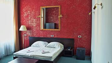 Una habitación de hotel con cama, mesitas de noche, escritorio, lámpara, espejo, calefacción y teléfono.