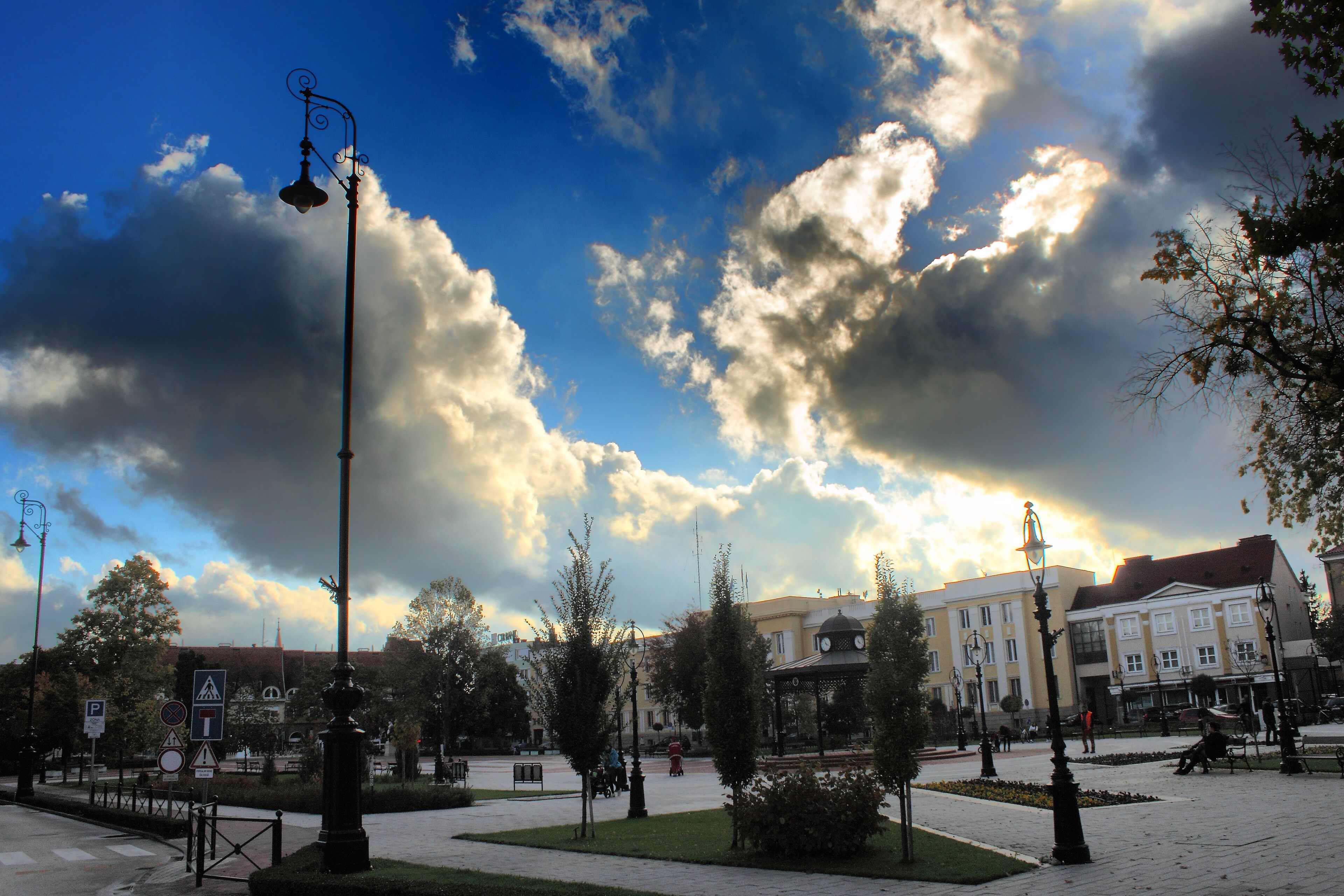 A public square with a gazebo, benches, and a clock tower in the background.