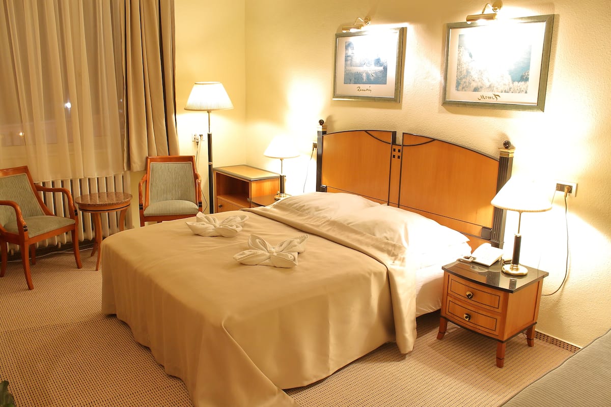 Quarto de hotel com uma cama, duas cadeiras, uma mesa de cabeceira e duas luminárias.