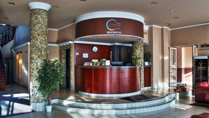 A hotel reception area with a curved reception desk, a clock, and a staircase leading to an upper level. - Hotel Centrál (Nagykanizsa)