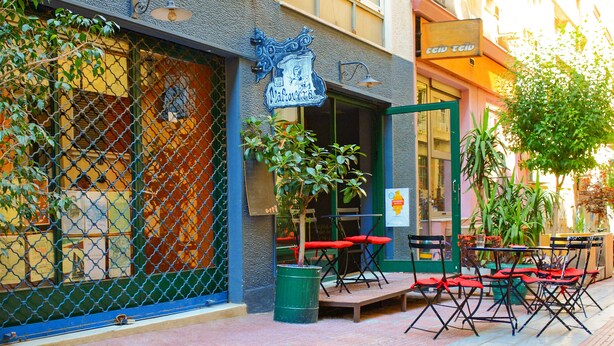 A cafe with outdoor seating, a chain-link fence, and a signboard. - Athens Connection Apartments (Athens)