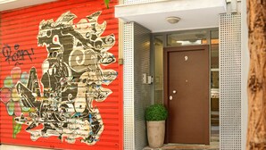 A building facade with a red door marked with the number 9, a metal perforated wall, and a potted plant near the entrance. - Athens Connection Apartments (Athens)