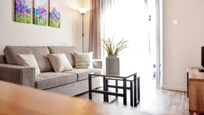 A living room with a grey sofa, a small table, and a potted plant. There are three abstract paintings on the wall and a lamp. - Athens Connection Apartments (Athens)