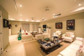 Uma sala de estar moderna com um sofá branco, uma mesa de centro com livros e uma televisão sobre um móvel.