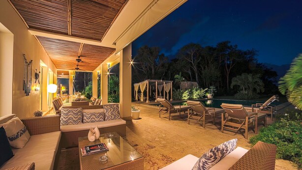 An outdoor lounge area with wicker furniture, a glass coffee table, and a pool in the background. - Hacienda B-03 (Punta Cana)