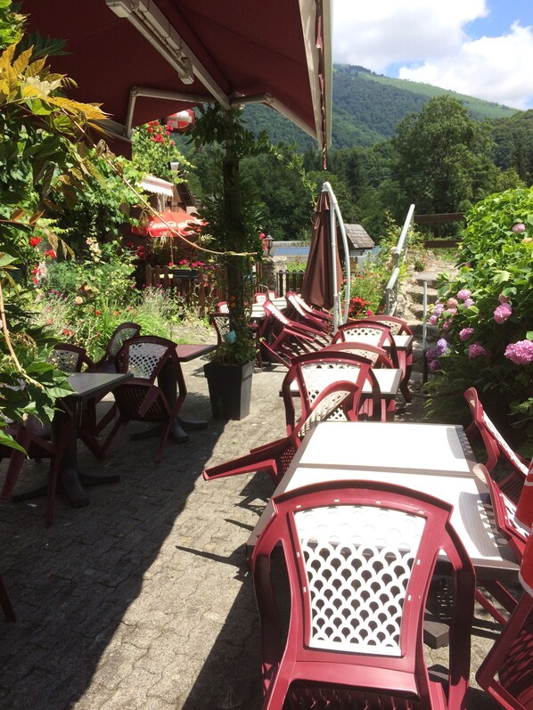 Un patio al aire libre con sillas y mesas de plástico rojo, rodeado de vegetación exuberante y flores.