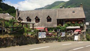 A hotel with a stone facade, multiple windows, and a sign indicating it offers a pension, bar, and restaurant. - Auberge des Pyrénées (Campan)