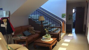 A living room with a sofa, a chair, a table with a vase, a teddy bear, and a staircase. - Auberge des Pyrénées (Campan)