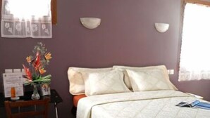 A bedroom with a bed, a nightstand, a vase with flowers, and a window with curtains. - Auberge des Pyrénées (Campan)