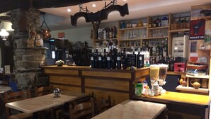 A restaurant with wooden tables and chairs, a stone wall, and shelves stocked with bottles and glasses. - Auberge des Pyrénées (Campan)