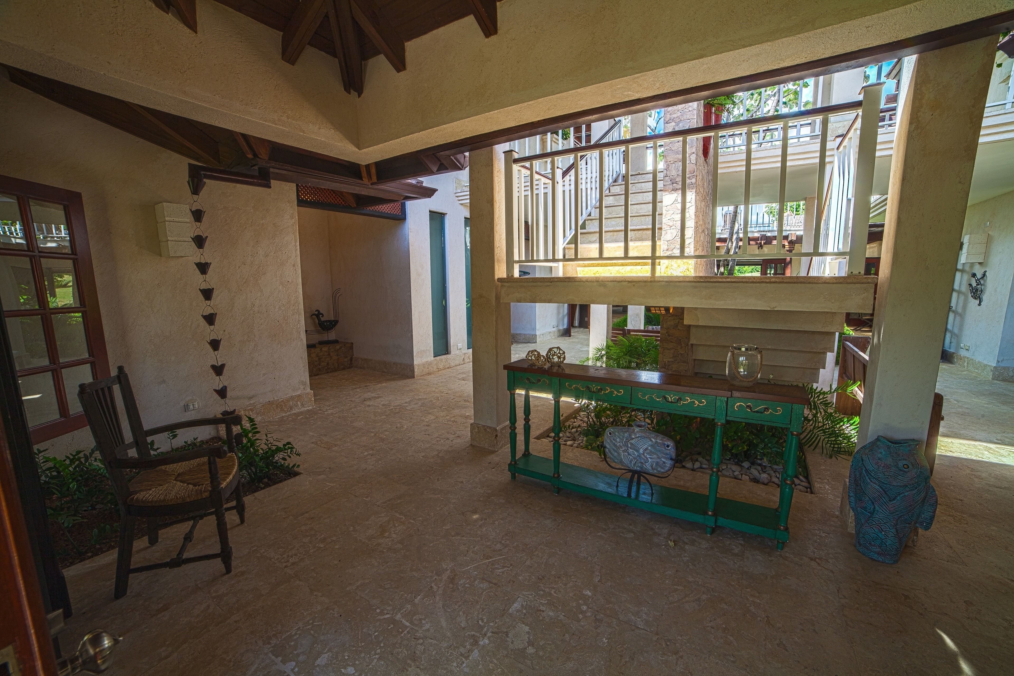 A spacious interior with a high ceiling, a wooden chair, a green console table, and a staircase leading to an upper level.