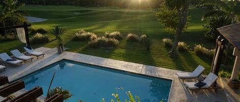 A pool area with lounge chairs and a view of a golf course.
