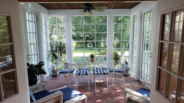 A sunroom with white wicker furniture, large windows, and a ceiling fan. - Miller-Dunham House Bed & Breakfast (Odessa)