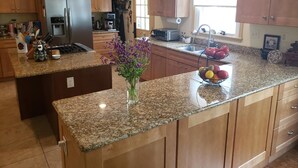 A kitchen with granite countertops, wooden cabinets, a refrigerator, a sink, and a ceiling fan. - Miller-Dunham House Bed & Breakfast (Odessa)