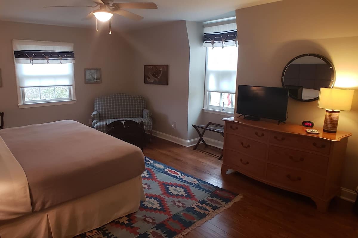 A hotel room with a bed, a dresser, a television, a chair, and a window with curtains.