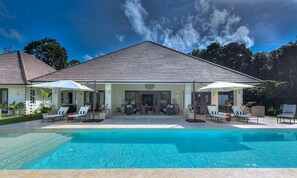 A two-story building with a swimming pool in front. There are lounge chairs and umbrellas around the pool. - Hacienda A-18 (Punta Cana)