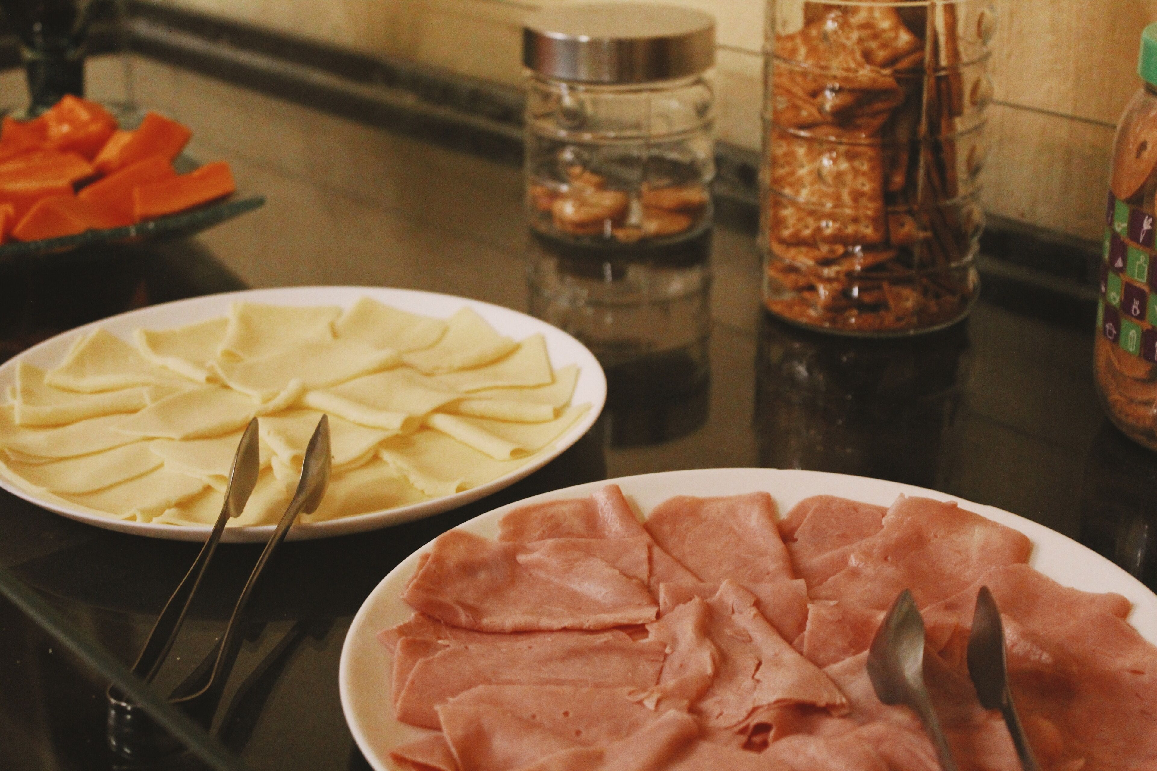 A table with plates of sliced cheese and ham, accompanied by serving utensils.