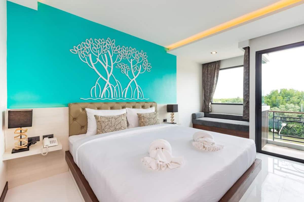 Una habitación de hotel moderna con una cama grande, una pared de acento color aguamarina y un balcón con vistas.