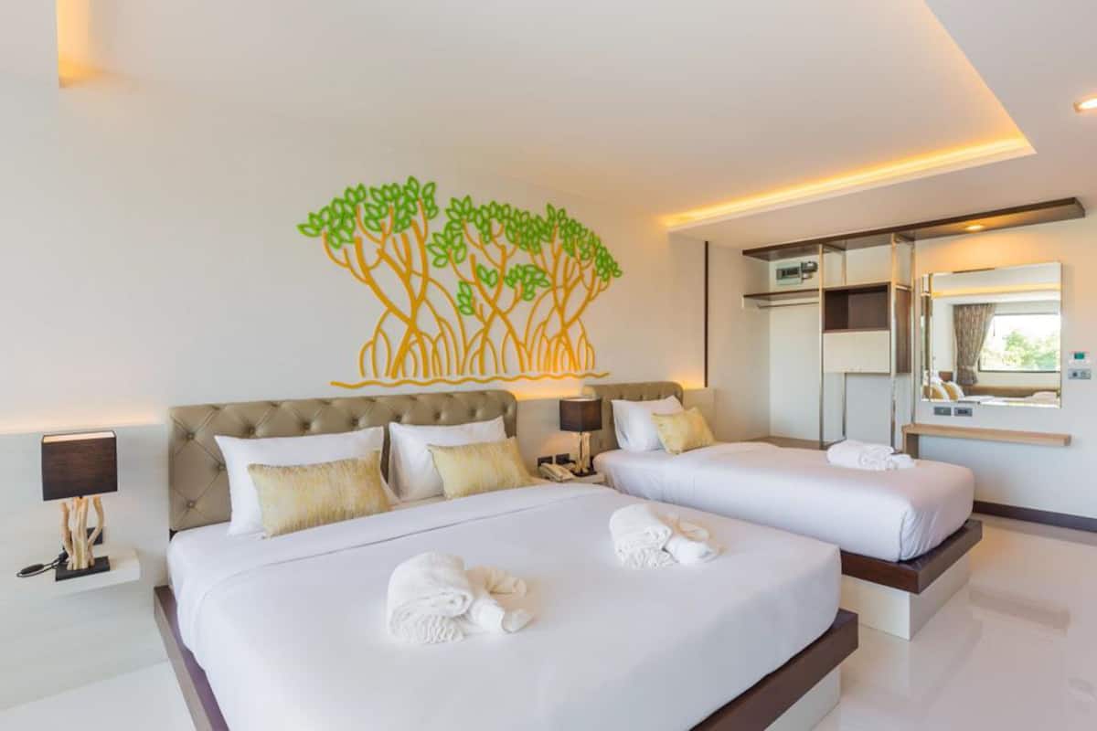 Habitación de hotel con una cama grande, dos mesitas de noche, un espejo y un cuadro de un árbol.