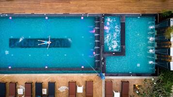An aerial view of a rectangular swimming pool with a tiled deck surrounding it. There are lounge chairs and a small section of the pool with a different tile pattern.