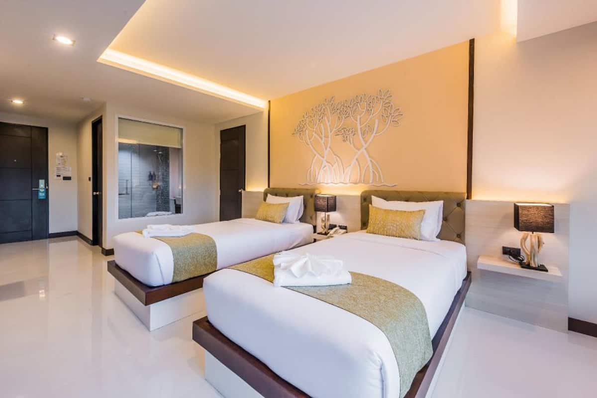 Habitación de hotel con dos camas, una gran obra de arte en la pared y un baño moderno visible a través de una puerta de cristal.