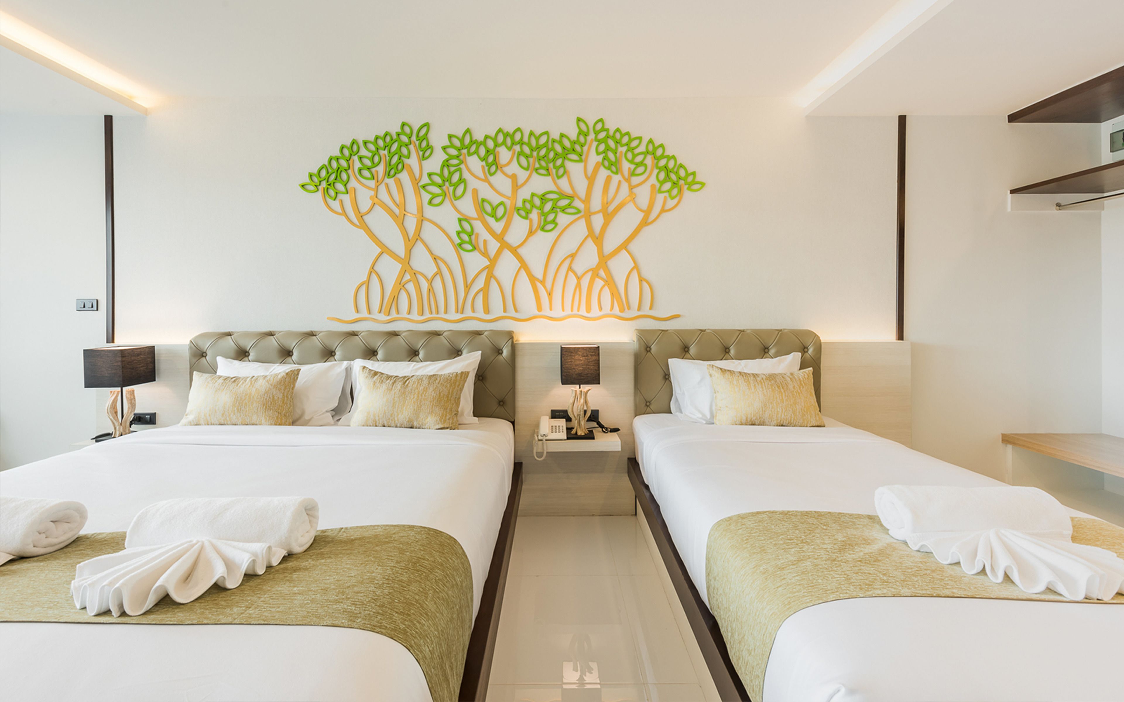 Una habitación de hotel con dos camas, una obra de arte en la pared que representa un árbol y una mesita de noche con una lámpara.