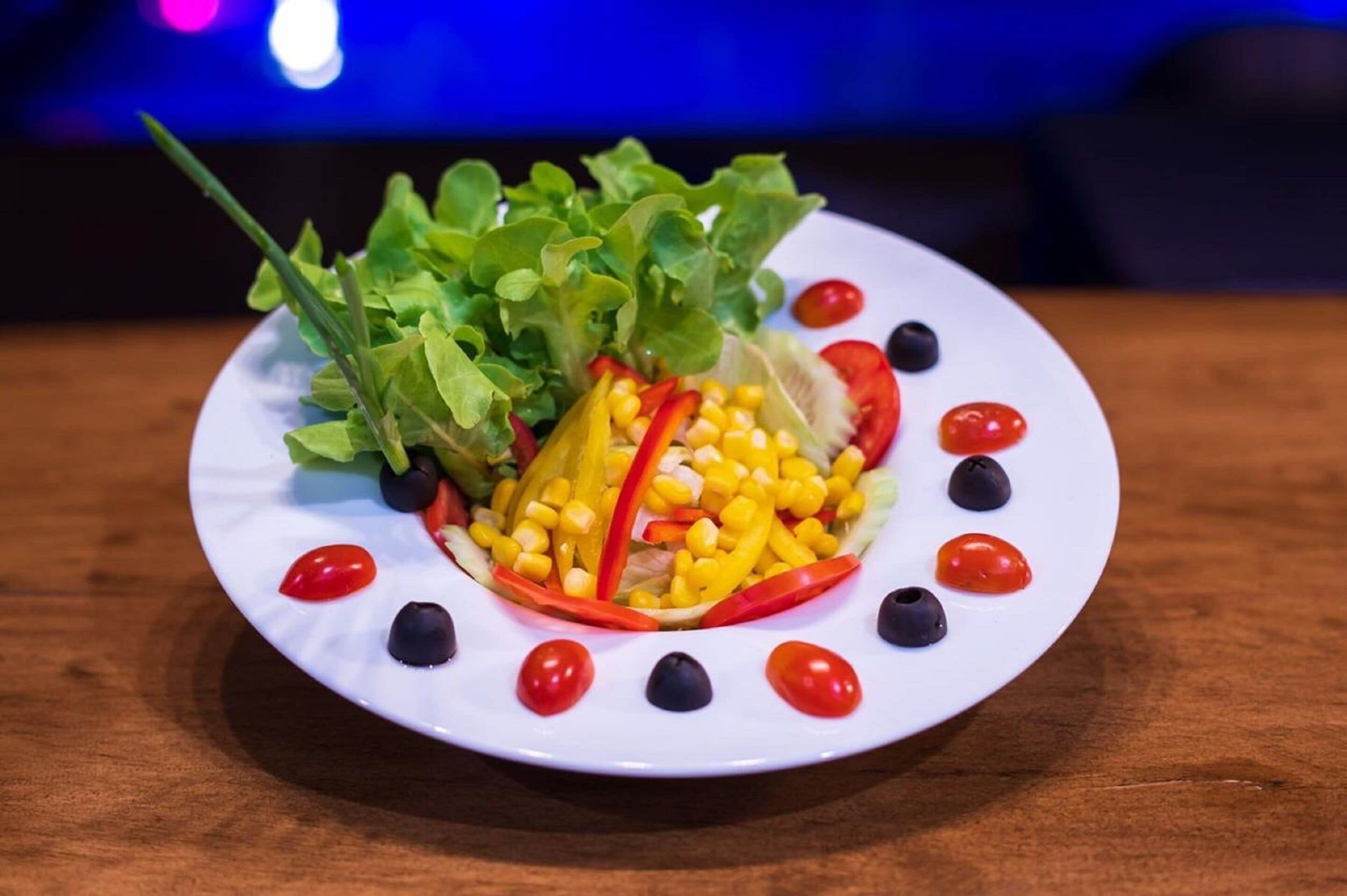 A plate of salad with various vegetables and a decorative arrangement of cherry tomatoes and olives.
