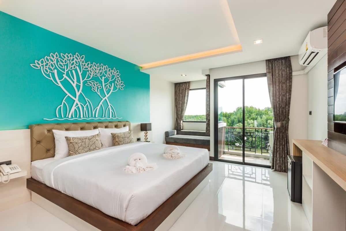 Una habitación de hotel moderna con una cama grande, un mural azul verdoso en la pared, un balcón con vistas y un televisor.