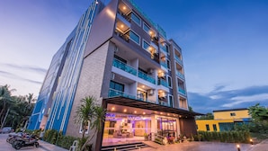 Um hotel de vários andares com design moderno, com varandas em cada andar, uma entrada bem iluminada e um estacionamento com scooters.