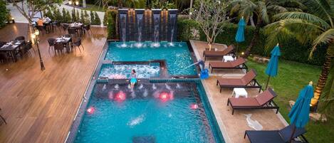A pool area with a waterfall feature, lounge chairs, and a dining area.