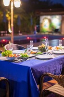 Een eettafel buiten gedekt, met een blauwe tafelkleed, borden, glazen en een mand met brood.