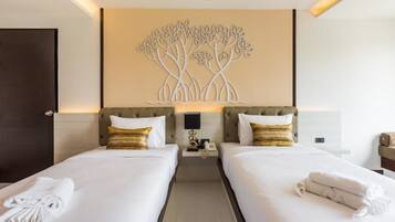 A hotel room with two beds, a wall-mounted artwork of trees, a bedside table with a lamp, and a phone.