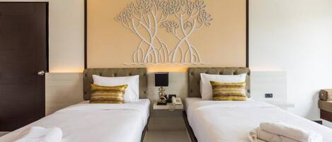 A hotel room with two beds, a wall-mounted artwork of trees, a bedside table with a lamp, and a phone.