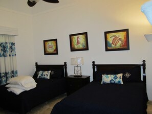 A hotel room with two beds, a nightstand with a lamp, and three framed seahorse paintings on the wall.
