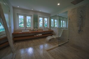 A modern bathroom with a large window, a glass shower enclosure, and a wooden vanity. - Arrecife 17 (Punta Cana)