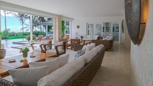 Un vaste espace de vie comprenant un grand canapé en osier, une table à manger avec des chaises et une vue sur l’extérieur.