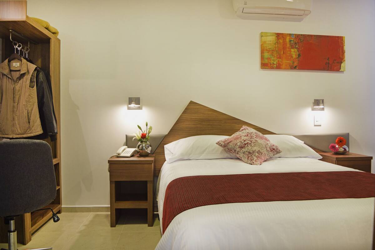 A hotel room with a bed, nightstands, a wooden wardrobe, and a wall-mounted artwork.