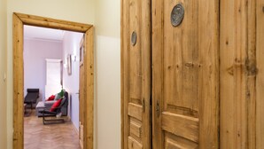 A wooden hallway with a door on the right and a sofa with a red cushion in the background. - KrakowRentals - Family Apartment (Kraków)