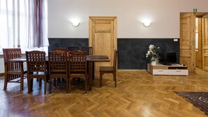 A dining area with a wooden table and chairs, a wooden door, and a television on a stand. - KrakowRentals - Family Apartment (Kraków)