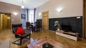 A living room with a black leather sofa, a wooden coffee table, a flat-screen TV, and a dining area with wooden chairs and a table. - KrakowRentals - Family Apartment (Kraków)