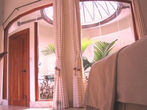 A room with a wooden door, a large window with curtains, and a view of palm trees outside.