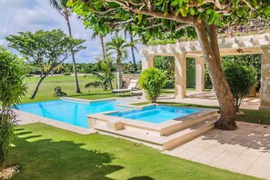 A swimming pool with a pergola and lounge chairs in a well-maintained garden.
