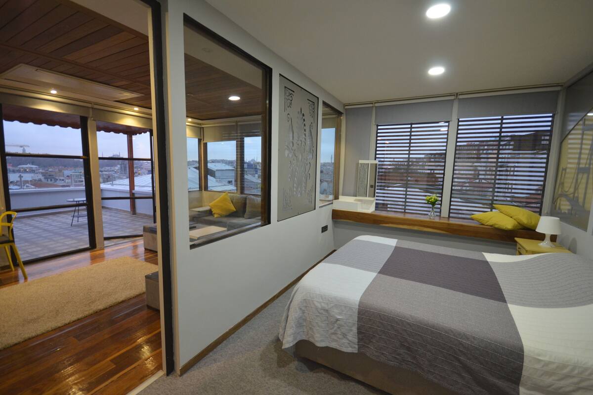 A modern bedroom with a large bed, a view of the city, and a sliding glass door leading to a balcony.