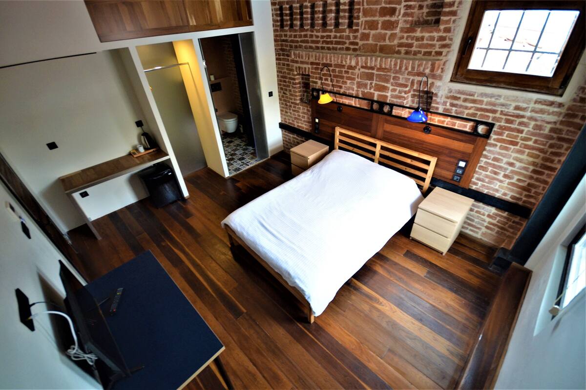 A bedroom with a bed, a wooden headboard, a nightstand, a dresser, and a brick wall.
