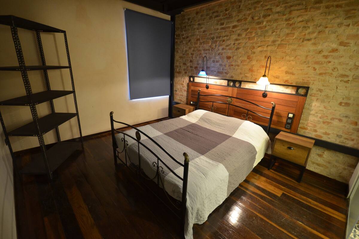 A bedroom with a metal bed frame, a wooden headboard, a nightstand, and a shelf unit.