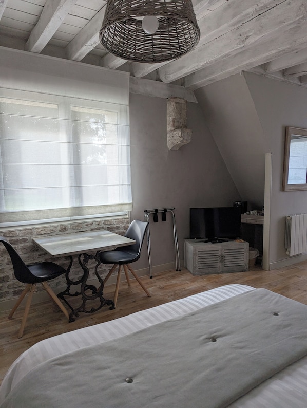 A cozy attic bedroom with a bed, a dining table with chairs, a TV, and a window with blinds. - Au Cocon de Sologne (Soings-en-Sologne)