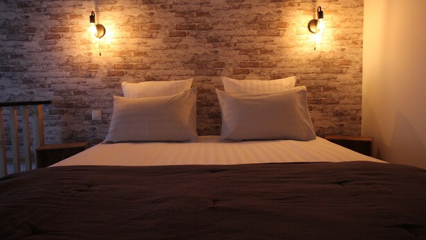 A bed with white linens and two pillows, a brick wall, and two wall-mounted lights. - Au Cocon de Sologne (Soings-en-Sologne)