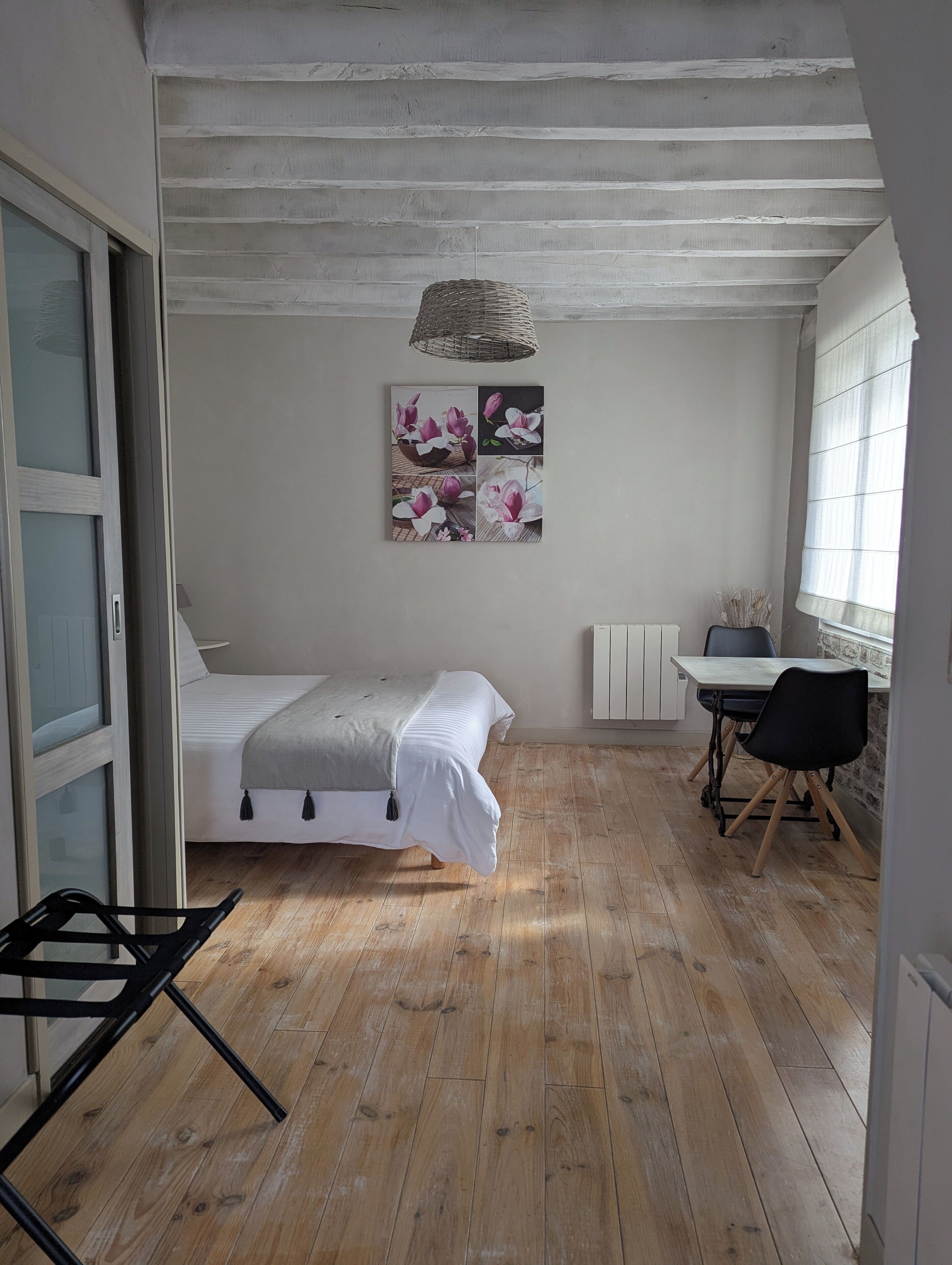 A bedroom with a bed, a desk, and a chair. There is a window with blinds and a radiator on the wall.