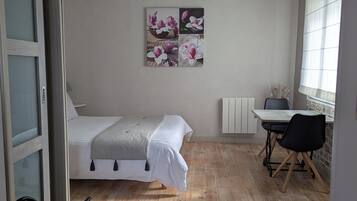 A bedroom with a bed, a desk, and a chair. There is a window with blinds and a radiator on the wall.