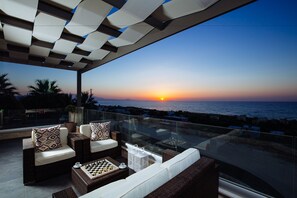A balcony with wicker furniture, a chessboard, and a sunset view. - Velvet Breeze Superior Villa (Rethymno)